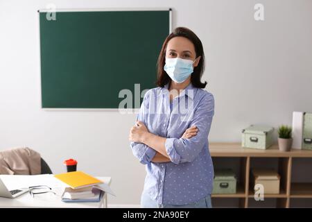 Lehrer mit Schutzmaske im Klassenzimmer. Wiedereröffnung nach Covid-19-Quarantäne Stockfoto