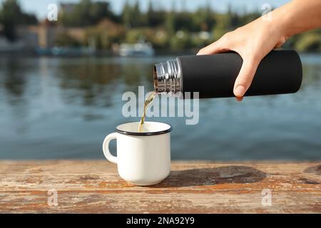 Eine Frau, die draußen heiße Getränke aus der Thermoskanne in den Becher gießt Stockfoto