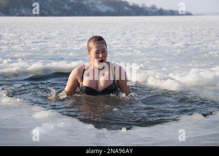 MYKOLAIV, UKRAINE - 06. JANUAR 2021: Frau, die am Wintertag in Eiswasser taucht Stockfoto