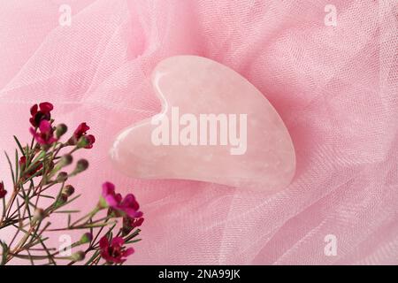 Rosenquarz Gua-Sha-Werkzeug und Blumen auf pinkfarbenem Stoff, flach liegend Stockfoto