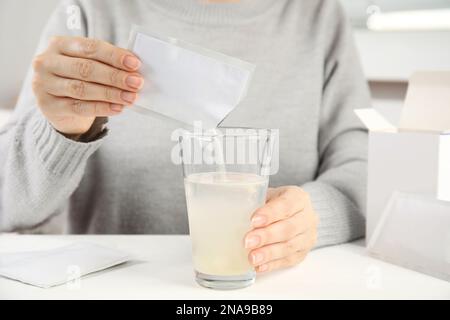Frau, die Pulver aus dem Arzneimittelbeutel in das Glas mit Wasser am Tisch gießt, Nahaufnahme Stockfoto