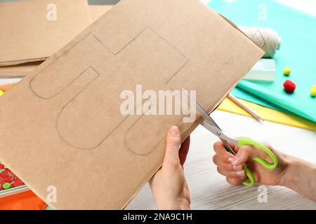 Eine Frau schneidet Kaktusform aus Papppapier auf einem weißen Holztisch aus, Nahaufnahme. Pinata Heimwerker Stockfoto