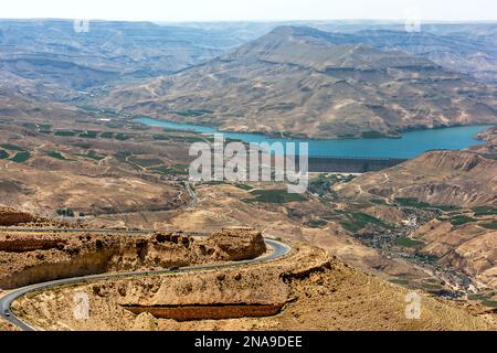 Ein Blick auf Wadi Mujib (Grand Canyon) mit der Mauer des Mujib-Staudamms. Neben dem Damm sind grüne Bewässerungsfelder zu sehen. Stockfoto