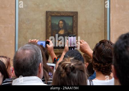 Touristen, die das berühmte Gemälde Mona Lisa fotografieren, das hinter kugelsicherem Glas im Louvre aufbewahrt wird; Paris, Frankreich Stockfoto