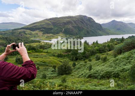 Ein Wanderer fotografiert die Berglandschaft und den See Loch Shiel in der Nähe von Glenfinnan, Schottland; Glenfinnan, Schottland Stockfoto