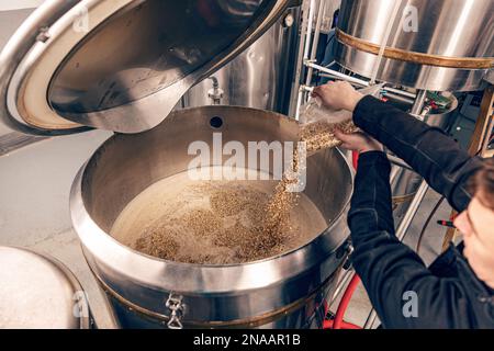 Der Arbeiter gießt Zutaten in ein Brühgefäß. Stockfoto