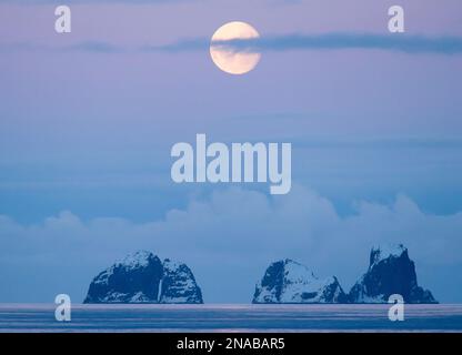 Vollmond untergeht über zwei bergige Inseln in der Gerlache-Straße vor der Küste der antarktischen Halbinsel, der Antarktis Stockfoto