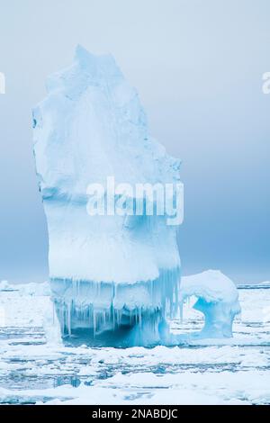 Ein ungewöhnlich geformter Eisberg schwimmt inmitten von Packeis im südlichen Ozean, direkt vor der Küste der Antarktischen Halbinsel; Antarktis Stockfoto