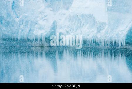 Schneeflocken fallen vor einem Eisberg, der mit Eiszapfen bedeckt ist; Antarktis Stockfoto