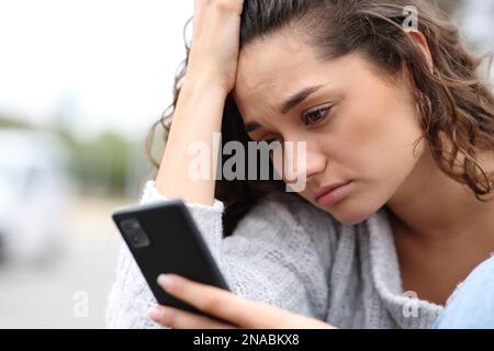 Traurige Frau, die auf der Straße ihre Nachricht überprüft und sich beschwert Stockfoto