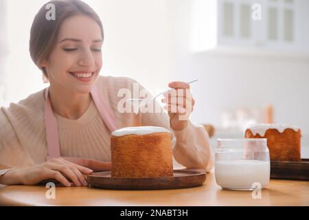 Junge Frau, die traditionellen Osterkuchen mit Glasur in der Küche dekoriert. Platz für Text Stockfoto