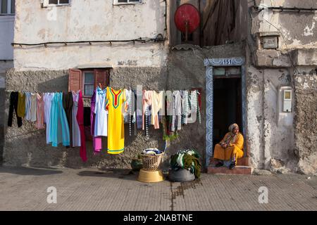 An einer Hauptstraße in Casablanca, Marokko, ruht eine Frau in der offenen Tür ihres Hauses, nachdem sie die Wäsche zum Trocknen aufgehängt hat; Casablanca, Marokko Stockfoto