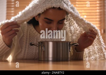 Eine Frau mit Karo, die über dem Topf inhaliert, an einem Tisch im Haus Stockfoto