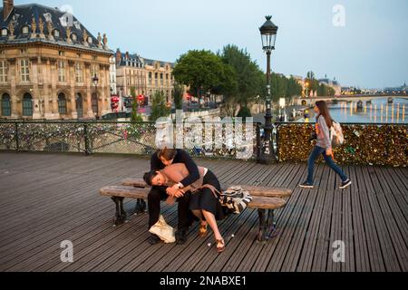 Bei Sonnenaufgang auf der Pont des Arts, oder der Love Lock Bridge, umarmt ein Paar auf einer Bank in Paris, Frankreich Stockfoto