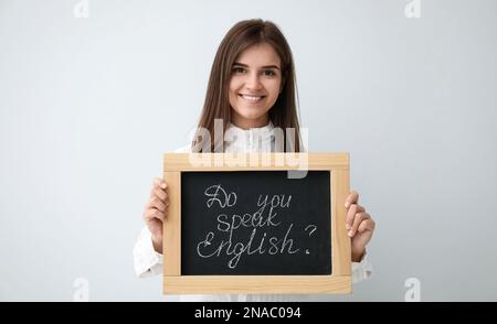 Junge Lehrerin mit Tafel und Wörtern Sprechen sie Englisch? Auf hellem Hintergrund Stockfoto