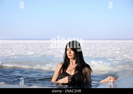 Frau, die am Wintertag in eiskaltes Wasser taucht. Taufe-Ritual Stockfoto