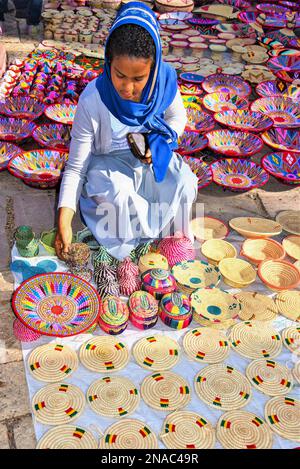 Frau, die äthiopisches Kunsthandwerk auf einem Markt kauft, mit einer Ausstellung auf dem Boden; Addis Abeba, Äthiopien Stockfoto