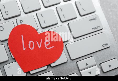 Papierherz mit Wort LIEBE auf Laptop, Nahaufnahme Stockfoto