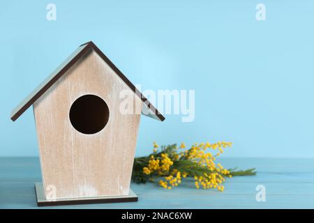 Wunderschönes Vogelhaus und Mimosablumen auf Holztisch vor hellblauem Hintergrund, Platz für Text Stockfoto