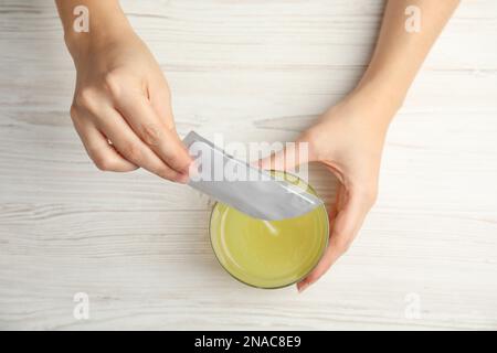 Frau schüttet Pulver aus dem Arzneimittelbeutel in Glas mit Wasser am Tisch, Draufsicht Stockfoto