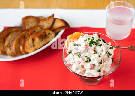 Würziger Krabbensalat in Glasschüssel, gebratener Toast und Limonade auf rotem Tischtuch auf dem Tisch. Stockfoto