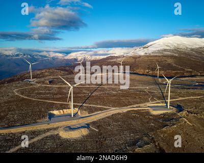 Windmühlen auf den Hügeln bei Sonnenuntergang. Erneuerbare Energien, grüne Energie. Berge im Hintergrund mit Schnee. Windkraft und umweltfreundlich. Stockfoto