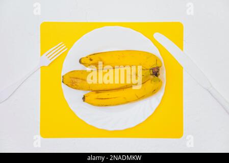 Reife gelbe Bananen auf einem weißen Teller. Layout, Ansicht von oben. Stockfoto
