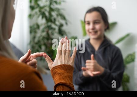 Kleines, kaukasisches Teenager-Kind Machen Sie zu Hause Artikulationsübungen mit einer fürsorglichen Mutter oder einer fürsorglichen Lehrerin. Das kleine Kind spricht Geräusche aus, spricht mit dem Lehrer oder Stockfoto