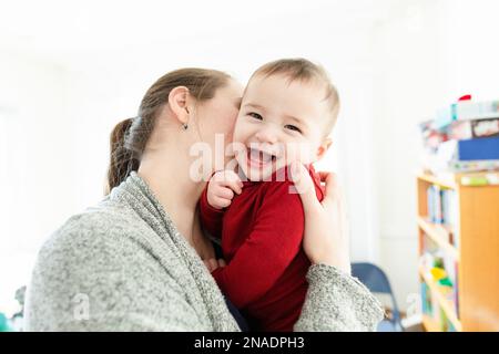 Mama umarmt und küsst lächelnden Baby Boy in roten Kleidern Stockfoto