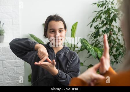 Kleines, kaukasisches Teenager-Kind Machen Sie zu Hause Artikulationsübungen mit einer fürsorglichen Mutter oder einer fürsorglichen Lehrerin. Das kleine Kind spricht Geräusche aus, spricht mit dem Lehrer oder Stockfoto