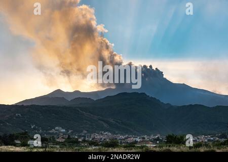 Dichte Wolken vulkanischer Asche, die aus den Kratern auf dem Ätna, Sizilien, emittiert werden, der über der Stadt Zafferana Etnea im Vordergrund thront Stockfoto