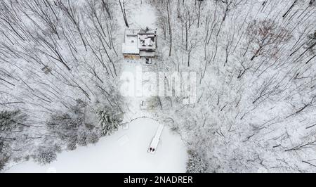 Luftblick auf Hütte und Dock an einem See an einem verschneiten Wintertag. Stockfoto
