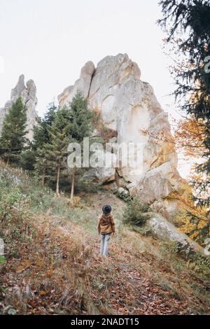 Eine Frau mit Jacke und Hut läuft durch den Wald in der Nähe der Berge Stockfoto