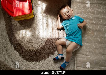 Der kleine Junge liegt auf dem Teppich neben der Matratze Stockfoto