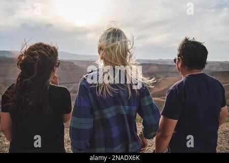 Drei Leute schauen vom Aussichtspunkt aus auf den Grand Canyon, windig Stockfoto