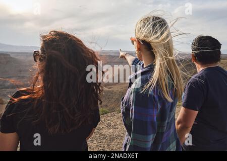 Drei Leute schauen vom Aussichtspunkt aus auf den Grand Canyon, windig Stockfoto