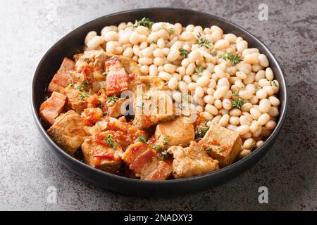 Spanisches Freginat ist ein Schweinefilet, das mit weißen Bohnen auf einem Teller auf dem Tisch serviert wird. Horizontal Stockfoto