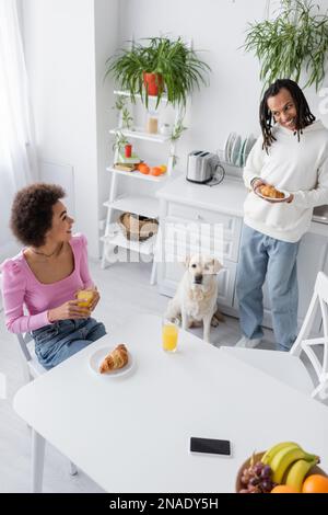 Blick aus der Vogelperspektive auf ein lächelndes afroamerikanisches Paar, das in der Nähe von labrador zu Hause frühstückt Stockfoto