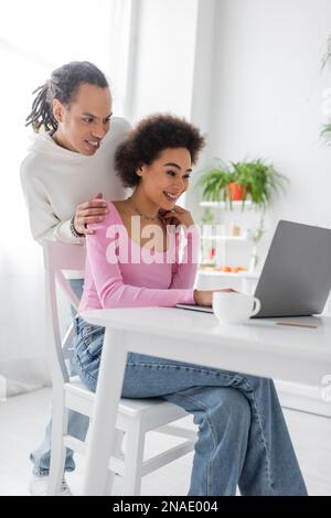 Lächelndes afroamerikanisches Paar, das in der Küche einen Laptop benutzt Stockfoto