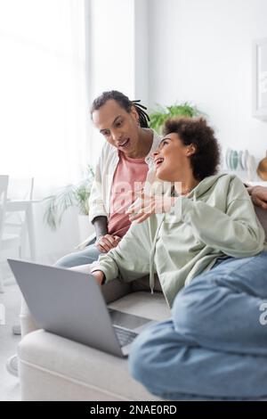 Eine afroamerikanische Frau, die mit ihrem Freund spricht, mit Dreadlocks in der Nähe des Laptops auf der Couch Stockfoto