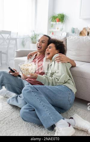 Aufgeregtes afroamerikanisches Paar mit Popcorn, das sich zu Hause Comedy-Filme ansieht Stockfoto
