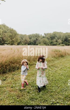 Zwei Mädchen gehen im Herbst an bewölkten Tagen durch das grasbedeckte Feld Stockfoto