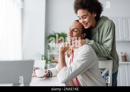 Junge afroamerikanische Frau, die ihren Freund zu Hause mit Kaffee berührt Stockfoto