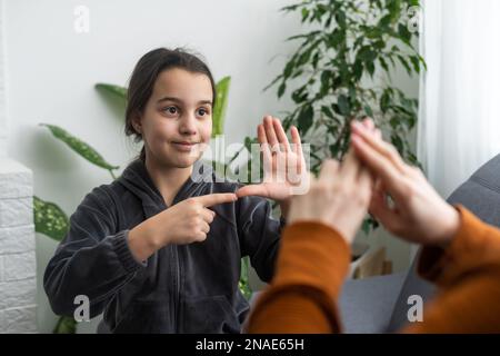 Kleines, kaukasisches Teenager-Kind Machen Sie zu Hause Artikulationsübungen mit einer fürsorglichen Mutter oder einer fürsorglichen Lehrerin. Das kleine Kind spricht Geräusche aus, spricht mit dem Lehrer oder Stockfoto