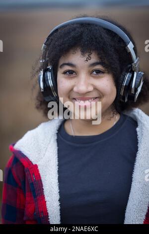 Ein birassisches Teenager-Mädchen, das Kopfhörer trägt und lächelt Stockfoto