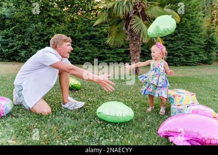 Baby spielt mit Dad in einem Ballon auf dem Gras Stockfoto