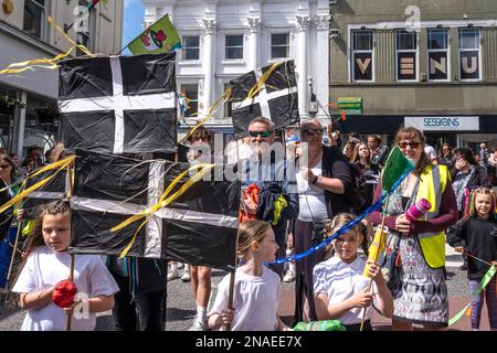 Erwachsene und Kinder, die an den farbenfrohen Mazey Day-Prozessionen in Cornwall, England, durch die Penazance fahren. Stockfoto