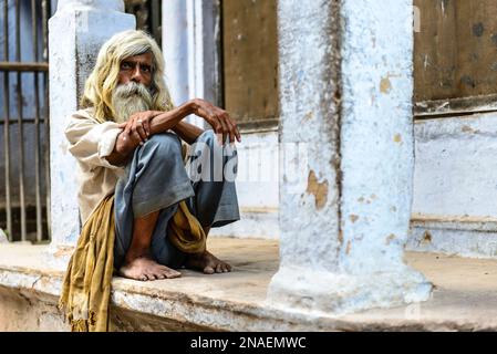 Sadhu lehnt sich an eine Säule vor einem Gebäude; Varanasi, Indien Stockfoto