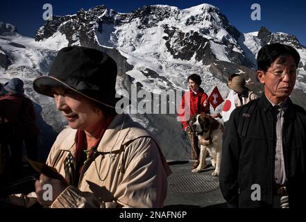 Japanische Touristen sehen das Matterhorn und posieren für Fotos mit den berühmten Bernhardiner-Hunden in den Alpen. Rund zwei Millionen Touristen besuchen jährlich ... Stockfoto