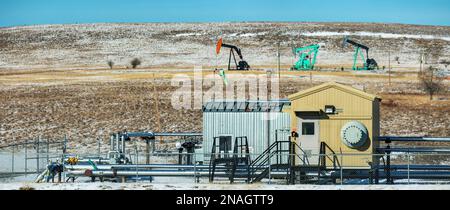 Kompressorstation mit Pumpjacks im Hintergrund, schneebedeckter Hügel mit blauem Himmel, nördlich von Longview, Alberta, Kanada Stockfoto